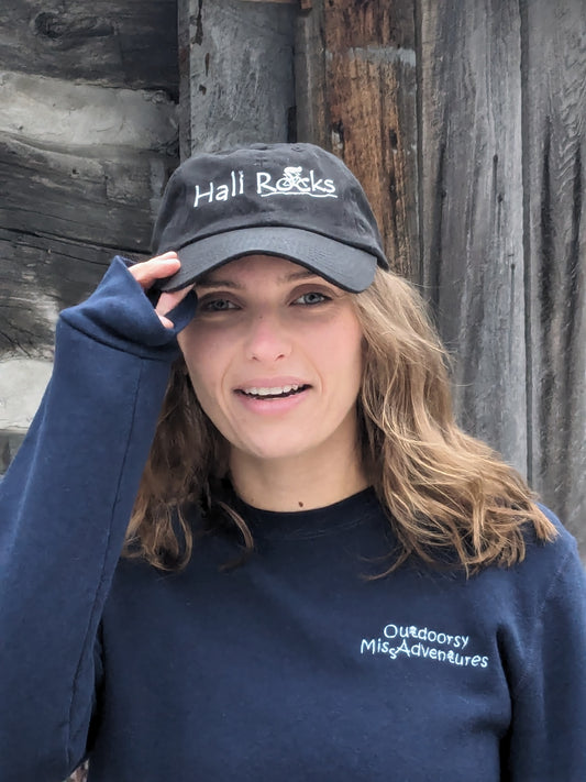 Small Town Natural model is wearing Hali Rocks Hat 100% Cotton regular curved peak colour = black, Embroidery = very light grey with cyclist climbing rocky trail