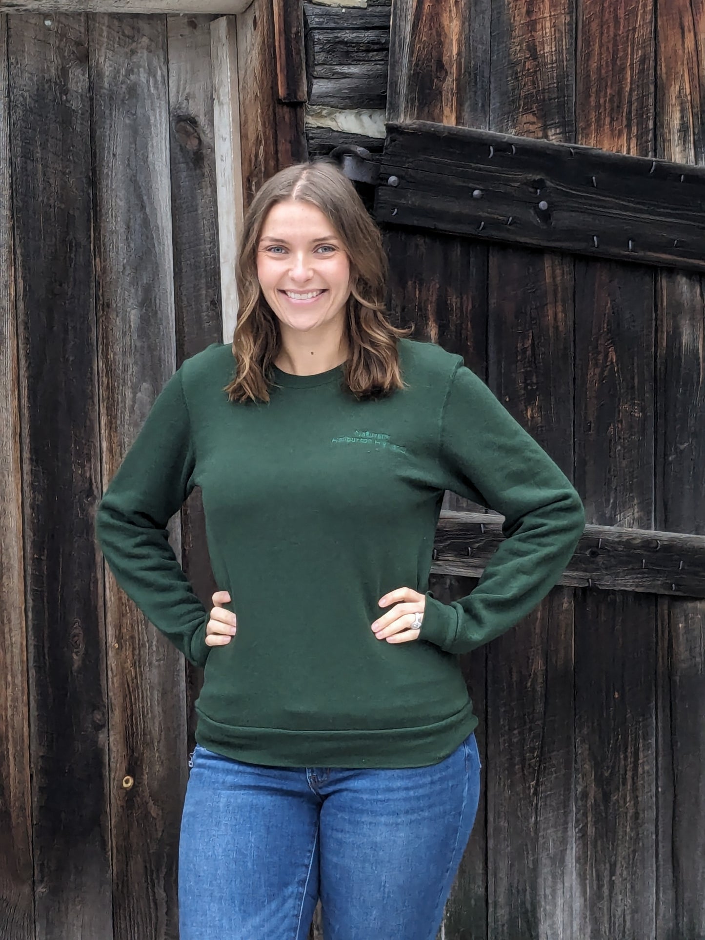 Naturally Haliburton Highlands in dark forest green subtle embroidery upper left chest. Forest green crew neck unisex sweatshirt.Small Town Natural model Morgan is wearing a Unisex size Small. She typically wears a size Medium in Women's sweatshirts.