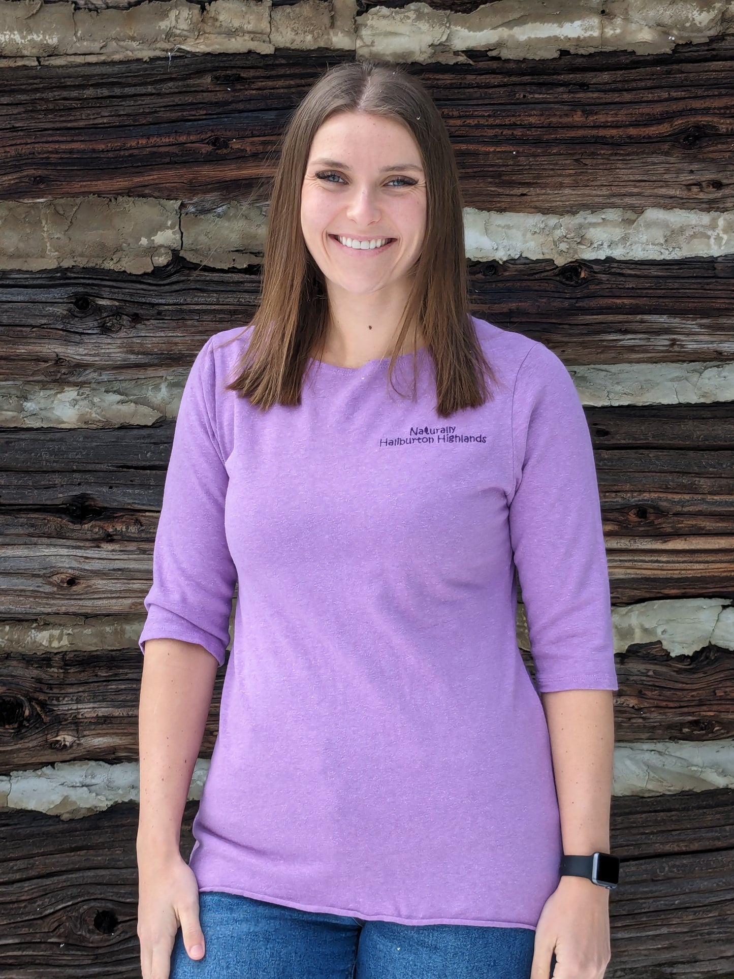 Naturally Haliburton Highlands words embroidered in dark grape purple thread on lilac coloured 3/4 sleeve hemp fluid top worn by our model Morgan